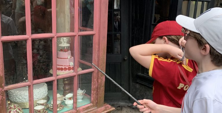 Two kids in Harry Potter gear point a wand at the Madam Puddifoot's tea shop window in the Wizarding World of Harry Potter